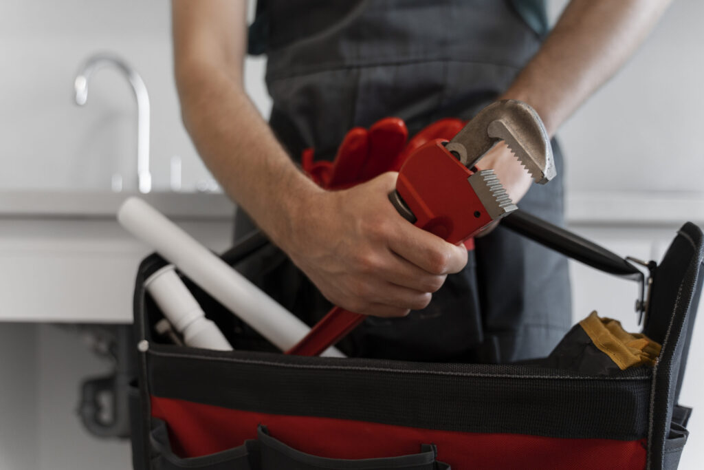 Mężczyzna trzyma narzędzie hydrauliczne, stojąc obok torby z akcesoriami w kuchni